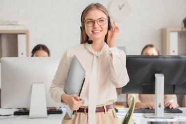 Kulaklık ve dizüstü bilgisayarlı bayan teknik destek ajanı ofiste.