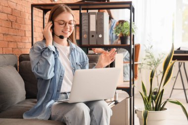 Ofisteki kanepede dizüstü bilgisayarla çalışan kadın teknik destek ajanı.