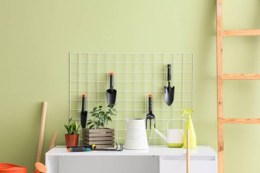 Atölyede yeşil duvarın yanında çivi tahtası ve bahçe aletleri olan çalışma yeri