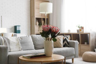 Oturma odasında üzerinde protea çiçekleri ve dergiler olan bir vazo.