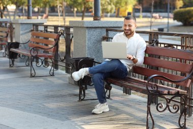 Park yerinde dizüstü bilgisayar kullanan yakışıklı genç adam.