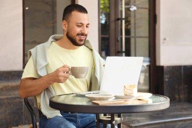 Cappuccino ve dizüstü bilgisayarlı genç adam sokak kafesindeki masada sohbet ediyor.