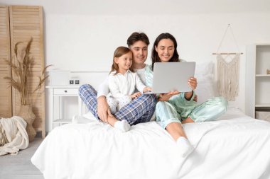 Ailesiyle yatak odasında dizüstü bilgisayar kullanan küçük bir kız.