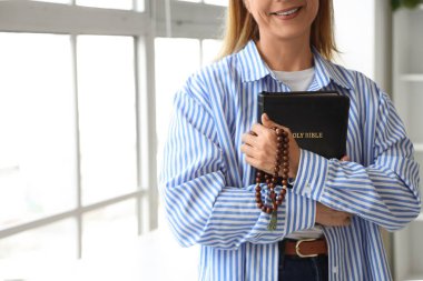 Evinin penceresinin yanında dua boncukları ve İncil 'i olan olgun bir kadın. Yakın plan.