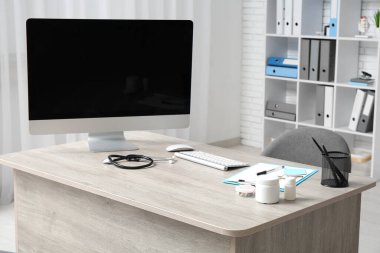 Ofisinde boş bilgisayar monitörü ve tıbbi gereçleri olan doktorun işyeri.