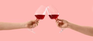 Pembe arka planda kırmızı şarap kadehlerini tokuşturan kadın elleri. 