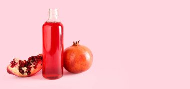Pembe zemin üzerinde bir şişe taze nar suyu ve metin için yer var.
