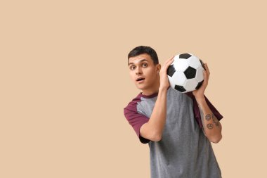 Bej arka planda futbol topu olan genç bir adam.