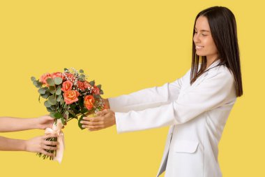 Sarı arka planda bir buket güzel çiçek alan genç kadın.