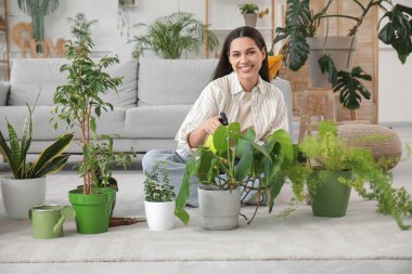 Genç bir kadın yerde oturup evdeki çiçekleri ilaçlıyor.