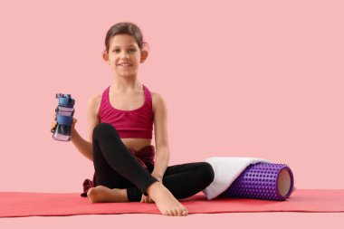 Su şişesi ve köpük silindirli küçük jimnastikçi pembe arka planda oturuyor.