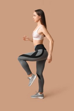 Genç bayan antrenör bej arka plan üzerinde egzersiz yapıyor.