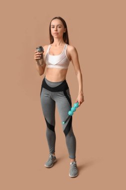 Bej arka planda bir şişe su ve vücut masajı yapan genç bir bayan antrenör.