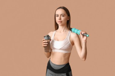 Bej arka planda bir şişe su ve vücut masajı yapan genç bir bayan antrenör.