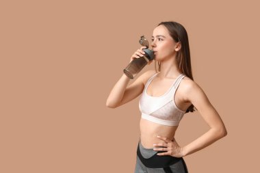 Genç bayan antrenör bej arka planda su içiyor.