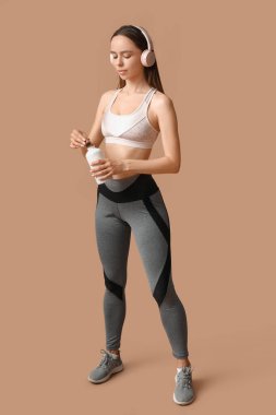 Bej arka planda bir şişe su ve kulaklığı olan genç bir bayan antrenör.