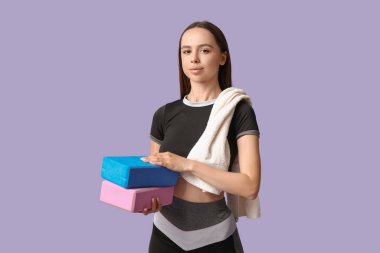 Leylak arka planında yoga blokları olan genç bir bayan antrenör.