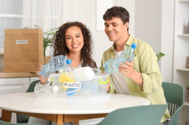 Genç bir çift mutfaktaki çöp konteynırına plastik şişe atıyor. Atık sıralama kavramı