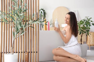 Evdeki banyoda şampuan şişeleriyle güzel, genç ve mutlu bir kadın.