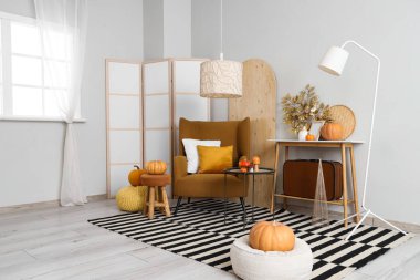 Sonbahar için tasarlanmış modern oturma odasının içinde rahat koltuklar, kahve masası ve balkabakları var.