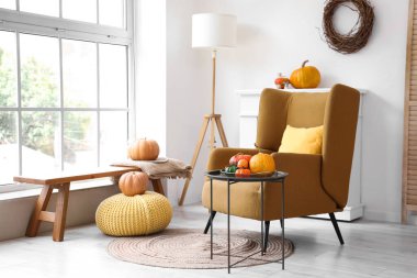 Sonbahar için tasarlanmış modern oturma odasının içinde rahat koltuklar, kahve masası ve balkabakları var.