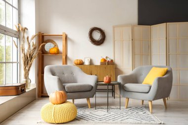 Sonbahar için tasarlanmış modern oturma odasının içinde rahat koltuklar, kahve masası ve balkabakları var.