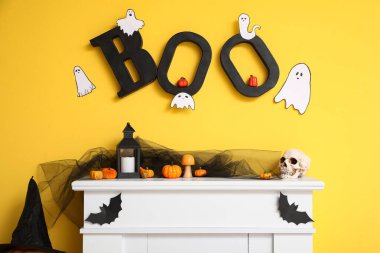 Oturma odasındaki sarı duvarın yanında Cadılar Bayramı süslemeleri olan şömine.