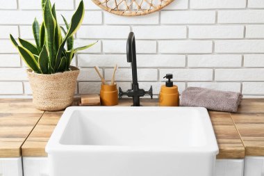 Banyo aksesuarları ve ev bitkisi banyoda beyaz tuğla duvarın yanında.