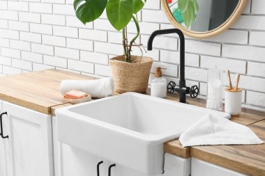 Banyo aksesuarları ve modern lavabo banyodaki beyaz tuğla duvarın yanındaki masada.