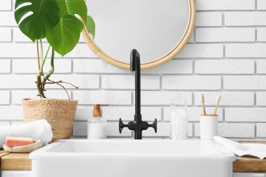 Banyo aksesuarları ve modern lavabo banyodaki beyaz tuğla duvarın yanındaki masada.