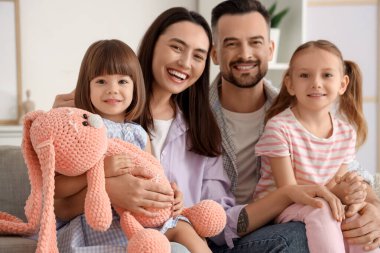 Evdeki kanepede oturan oyuncak tavşanlı mutlu bir aile.