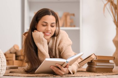 Güzel, genç, mutlu bir kadın evde kitap okuyor.