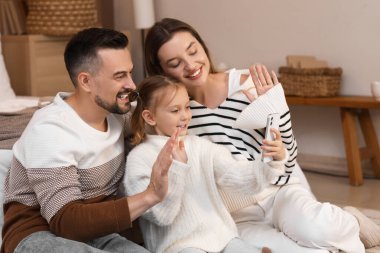 Mutlu ebeveynler ve cep telefonlu küçük kızları kış akşamı evde cep telefonlarıyla sohbet ediyorlar.
