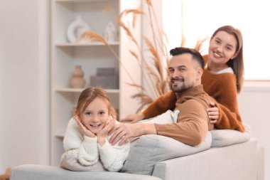 Mutlu ebeveynler ve küçük kızları kış günü evde kanepede oturuyorlar.