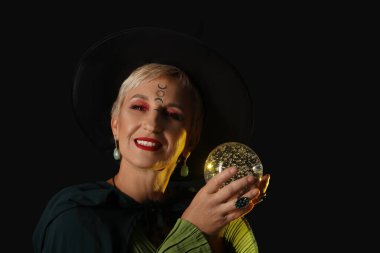 Mature witch with crystal ball on dark background, closeup