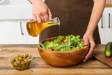 Mutfaktaki masada lezzetli salata ile zeytinyağı ekleyen bir kadın.