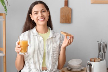Bir bardak portakal suyuyla genç ve güzel bir kadın mutfakta fıstık ezmeli tost yiyor.