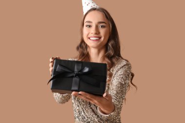 Parti şapkalı güzel bir kadın kahverengi arka planda doğum gününü kutluyor.