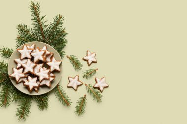 Yeşil arka planda yıldız şeklinde zencefilli kurabiye ve köknar dallarıyla kaplı bir tabak.