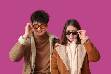 Mor arka planda güneş gözlüklü şık elbiseli güzel bir çift.