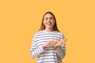 Young deaf mute woman using sign language on orange background