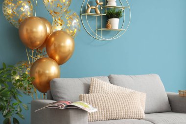 Modern oturma odasındaki mavi duvarın yanında rahat bir kanepe ve altın hava balonları.