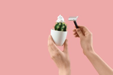 Pembe arka planda jilet, kaktüs ve köpüklü kadın elleri.