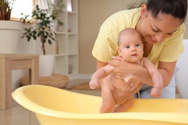 Güzel, genç, mutlu bir anne ve evde banyo yapan şirin bir bebek.