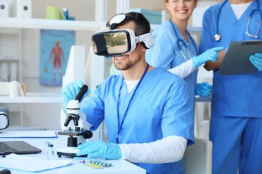 Klinikteki masada mikroskop kullanan erkek doktor.