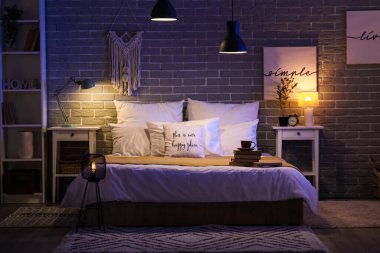 Karanlık yatak odasının içinde gece lambaları, kahve fincanı ve yatağında kitaplar vardı.