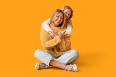 Güzel kadın ve şık süveter giyen tatlı kızı sarı arka planda oturuyor.