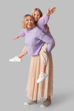 Gri arka planda leylak rengi süveterler içinde güzel bir kadın ve tatlı kızı var.