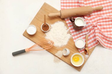 Beyaz arka planda tatlı tarçınlı rulo hazırlamak için farklı malzemeler içeren ahşap tahta tahta.