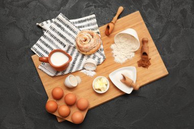 Siyah arka planda tatlı tarçınlı rulo hazırlamak için farklı malzemeler içeren ahşap tahta tahta.